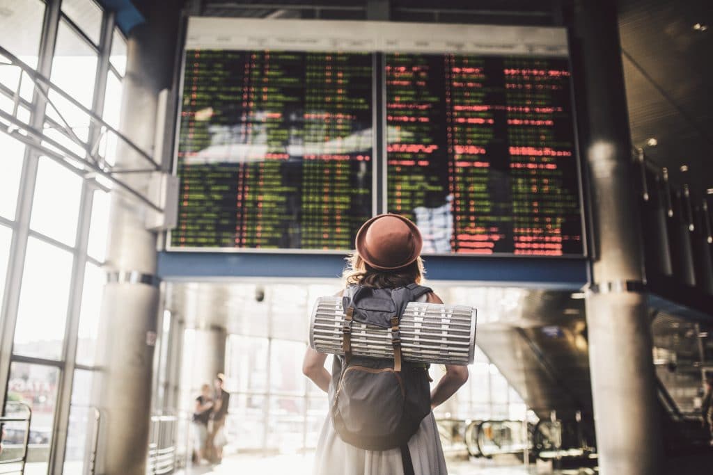 Eine junge Frau mit rotem Hut steht vor der Anzeigetafel an einem Flughafen