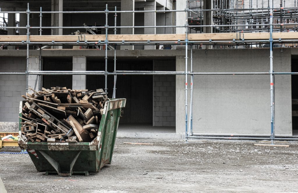 Ein Container gefüllt mit Bauschrott steht vor einem Haus auf einer Baustelle